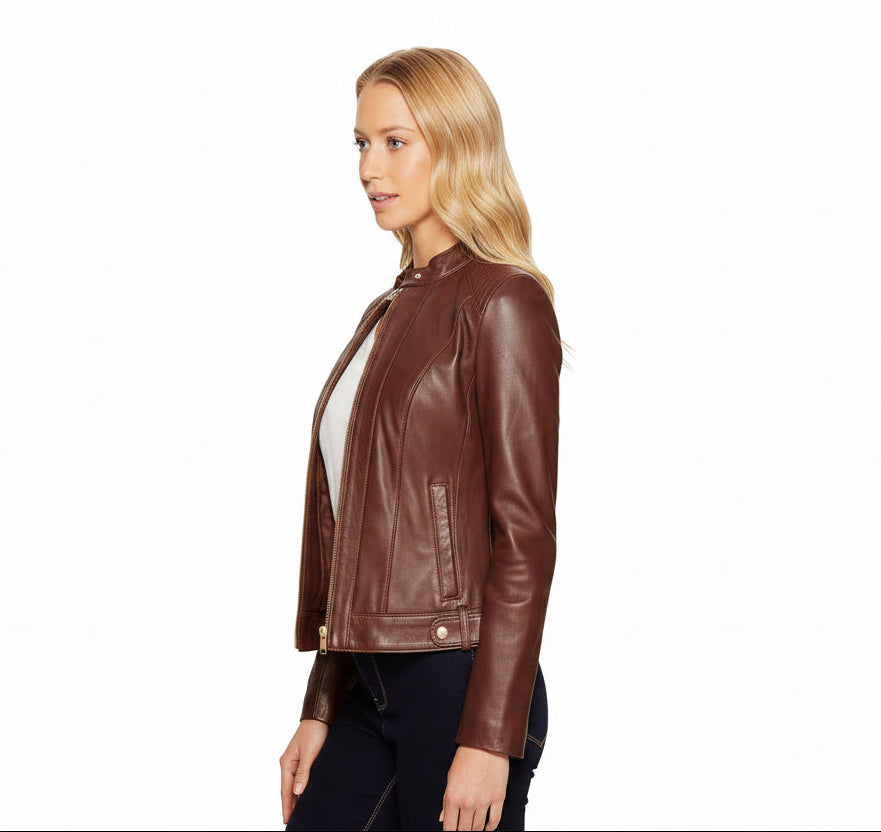 A blonde woman wearing a brown-leather moto jacket over a white top and black jeans, photographed against a solid white background.