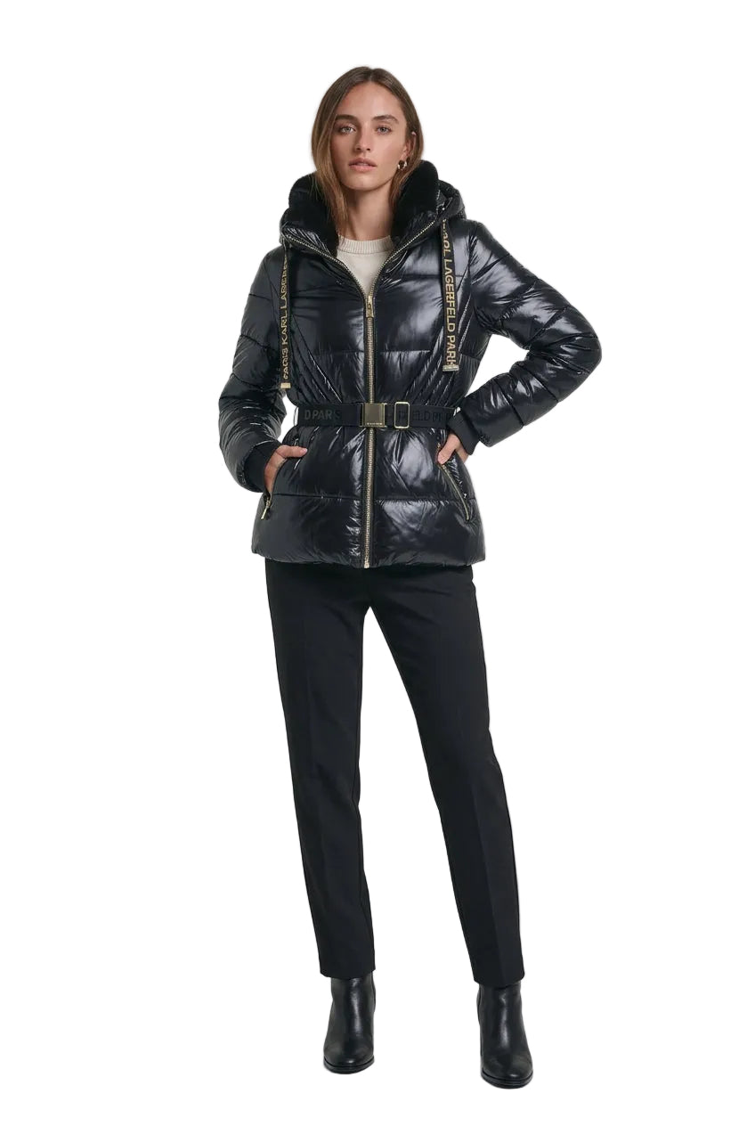 A woman wearing a shiny black puffer jacket with a fur-trimmed hood, gold-tone zipper, and a matching black belt with gold lettering
