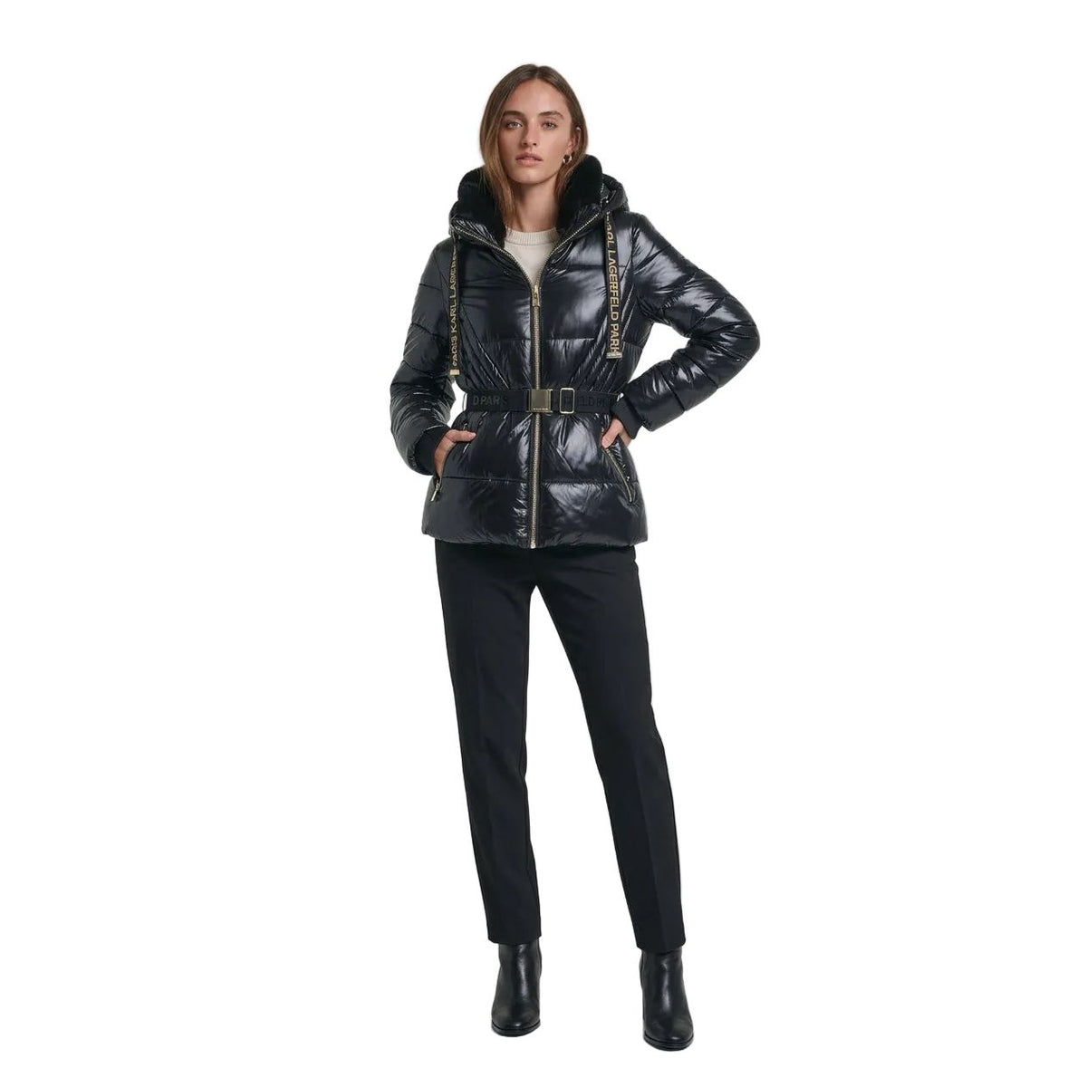 A woman wearing a shiny black puffer jacket with a fur-trimmed hood, gold-tone zipper, and a matching black belt with gold lettering